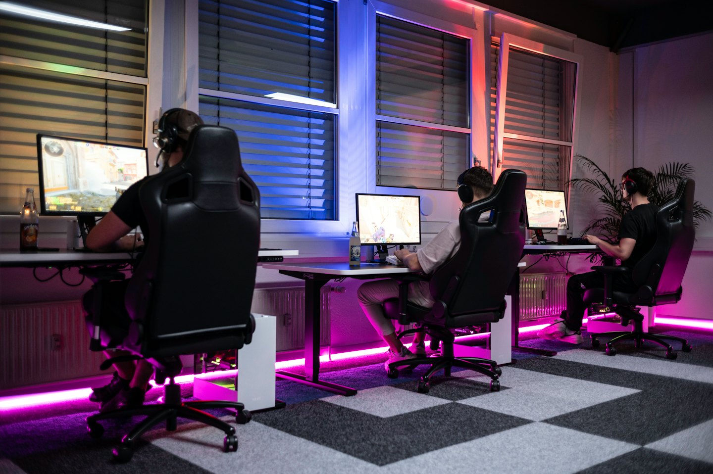 Trois personnes jouant à des jeux vidéo sur des ordinateurs dans une pièce lumineuse.