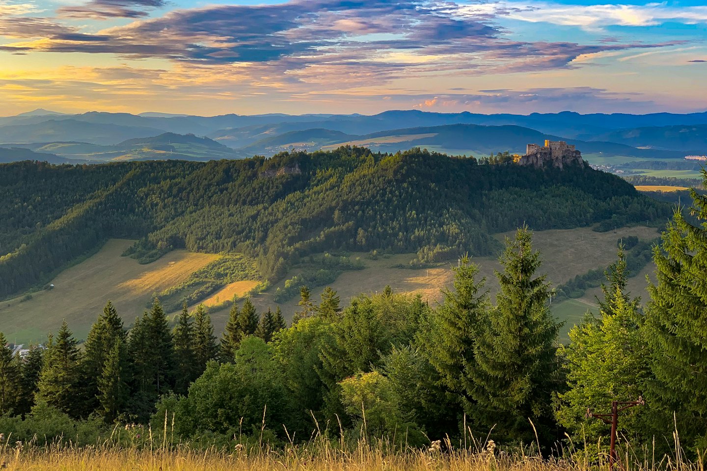 Château médiéval sur une colline boisée au coucher du soleil.