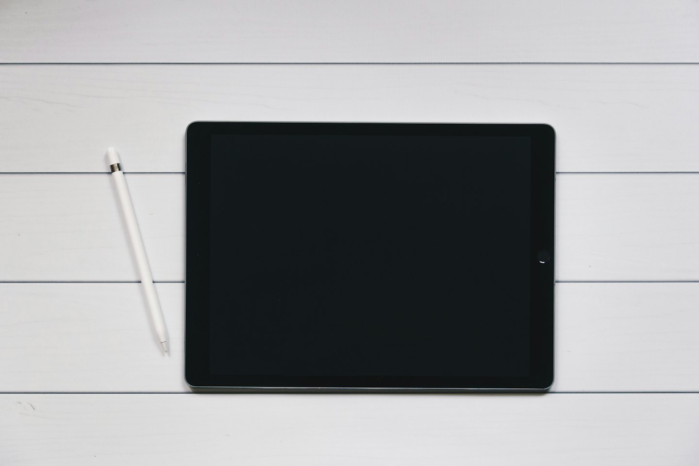 Tablette noire et stylet blanc sur une planche en bois.